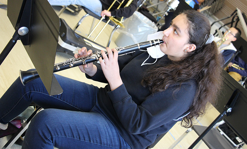 A fifth-grade girl with long dark hair, wearing a navy blue shirt, plays a clarinet.