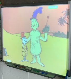 A screen with two dr. seuss characters on it. One is holding a ham.