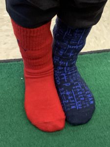 Feet wearing two different socks - one on the left is read and the one on the right is blue print.