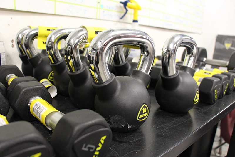 Many kettlebells, black with silver metal handles on a shelf.