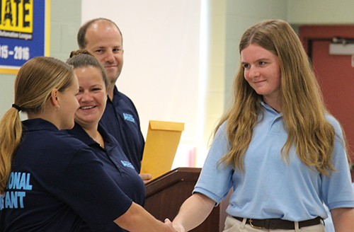 A young woman with long blonde hair shakes hands with another woman .