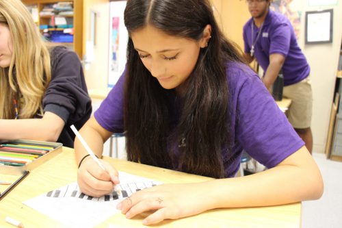 A young woman with long dark hair draws piano keys on a piece of paper.
