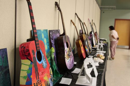 Several painted guitars stand on a table and lean up against a wall.