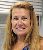 A woman with long blonde hair, wearing a blue shirt, smiles.