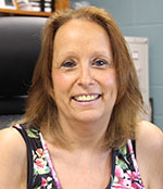 A woman with shoulder length reddish hair smiles. She is wearing a flowered tank top.