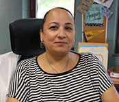 A woman smiles. She is wearing a black and white striped short-sleeve shirt and her hair is pulled back.