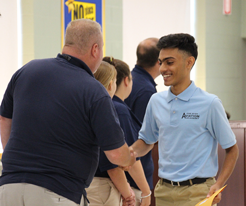 A young man with short dark hair shakes hands with a man wearing a dark blue shirt.