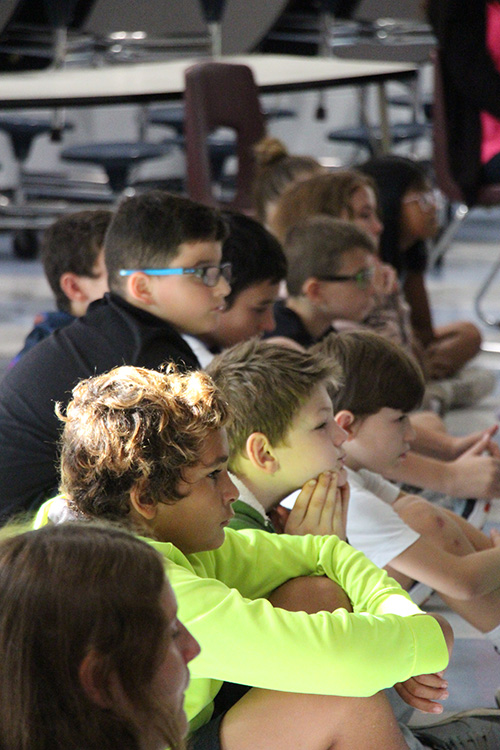 A row of 10 fifth-grade students sitting on a floor.