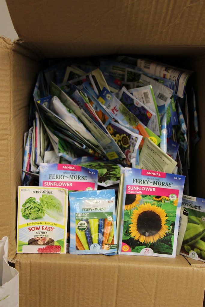 A brown cardboard box filled with a thousand packets of seeds for flowers, fruits and veggies.