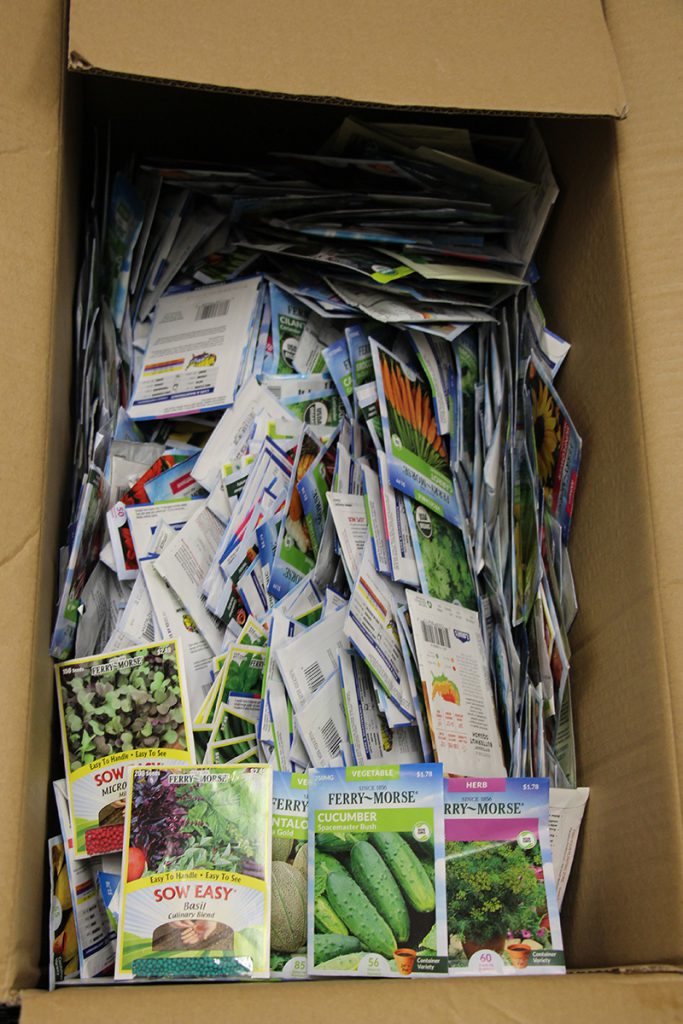 A large brown cardboard box filled with a thousand packets of vegetable fruit and flower seeds.