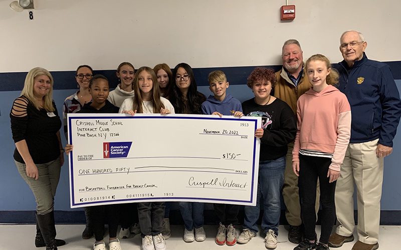 A group of middle school students stand with five adults. A student in front is holding a large ceremonial check for $150 made out to the American Cancer Society.