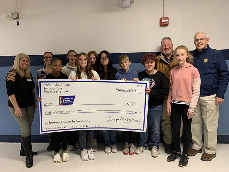 A group of middle school students stand with five adults. A student in front is holding a large ceremonial check for $150 made out to the American Cancer Society.