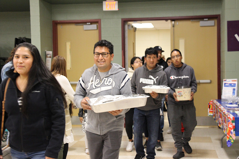 A steady stream of adults come in through the door, each carrying a covered dish of food.