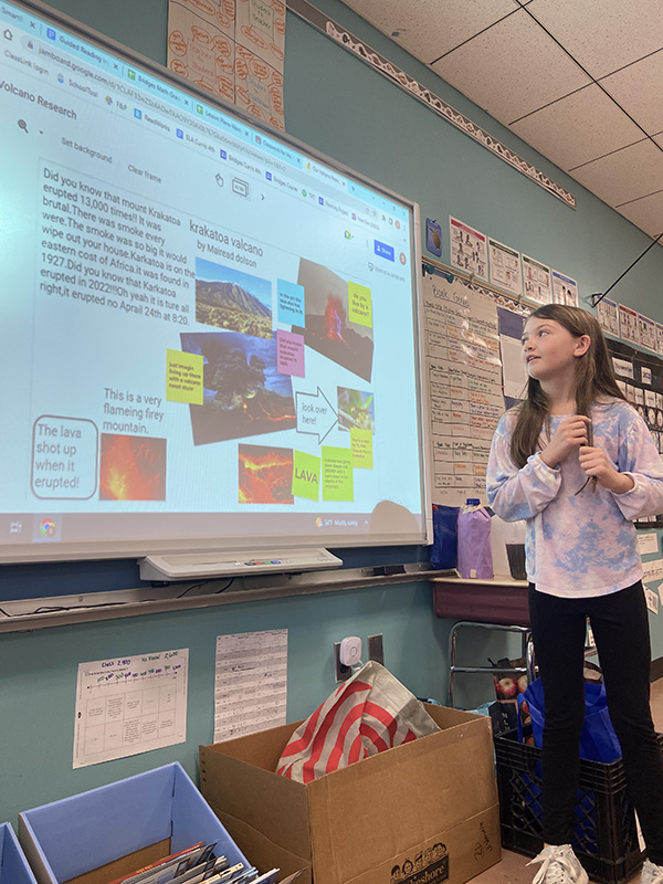 A student stands in front of a white board with a presentation on it.