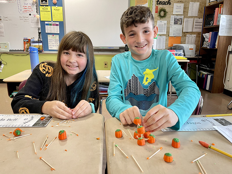 Two fifth grade students, a girl on th eleft and a boy on the right, work on a project using toothpicks and small candy pumpkins.
