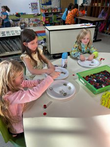 Three elementary girls sit at a table with plates in front of them sorting items onto the plates.