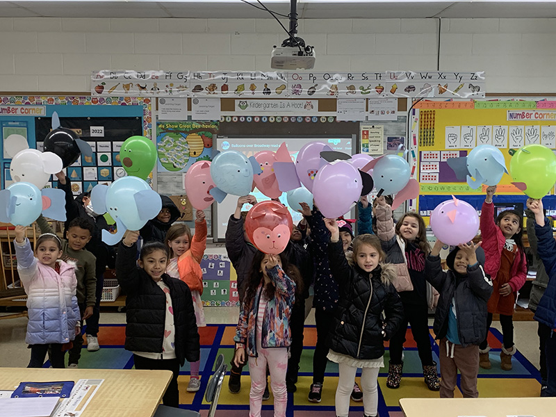 A large group of kindergarten students stand together holding their balloons.