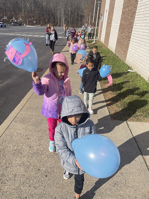 A parade of students, all wearing winter jackets, holding up their decorated balloons.