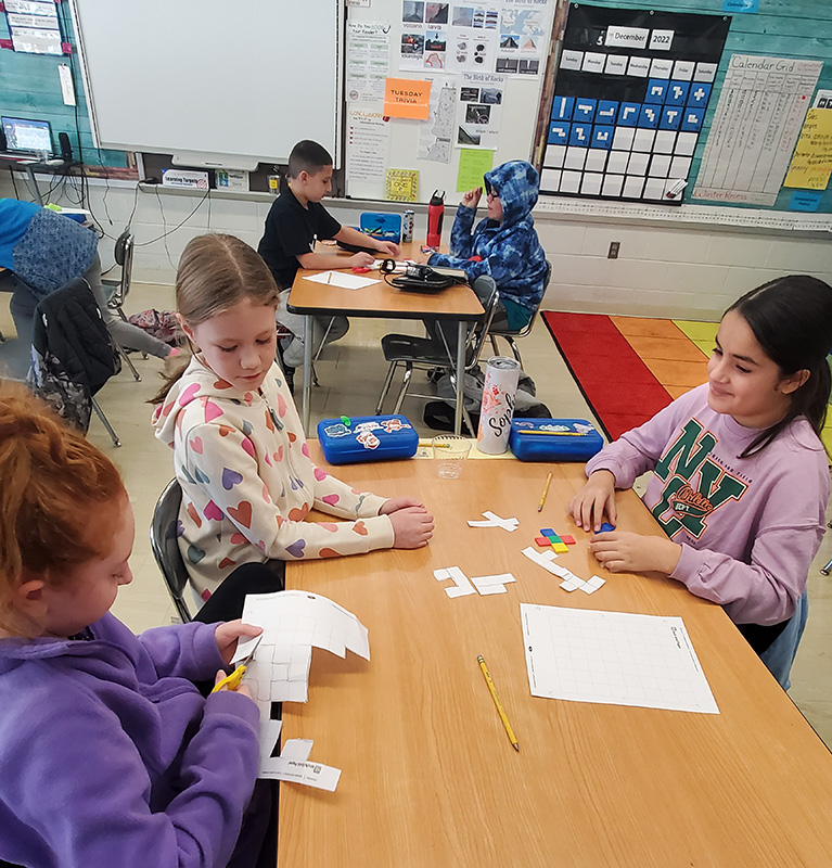 Three fourth-grade girls sit at a table working with white blocks.