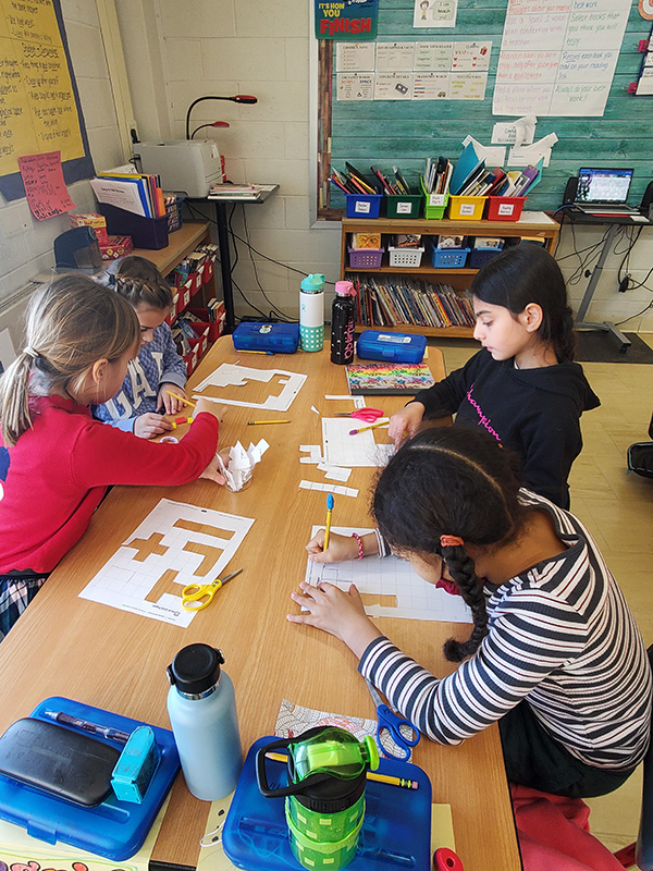 Four fourth-grade students work together with white blocks at a big table.