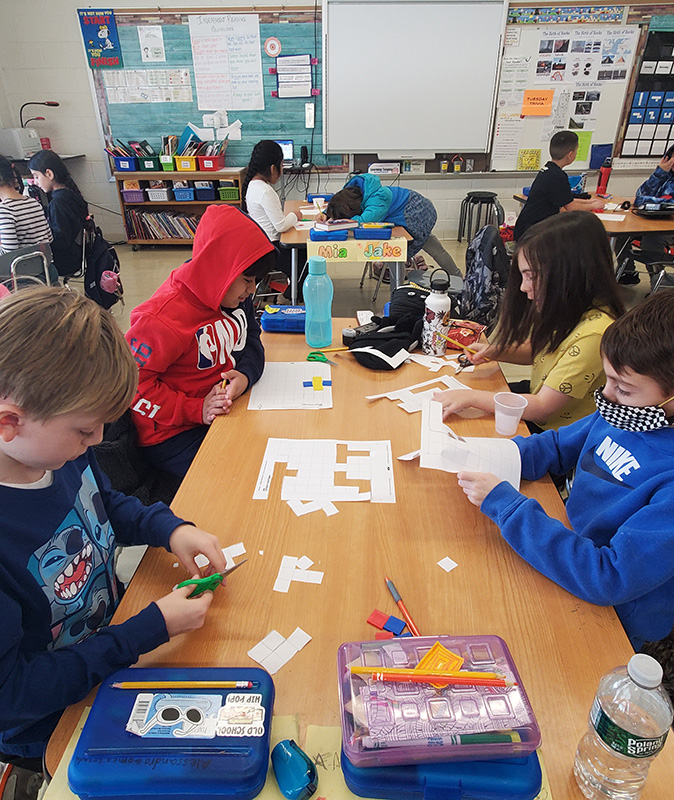 A small group of fourth-grade students work at a table with white blocks.