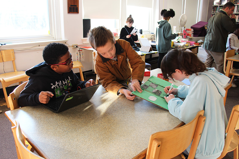 Three sixth-grade kids work on a chromebook and a board where one student is drawing.