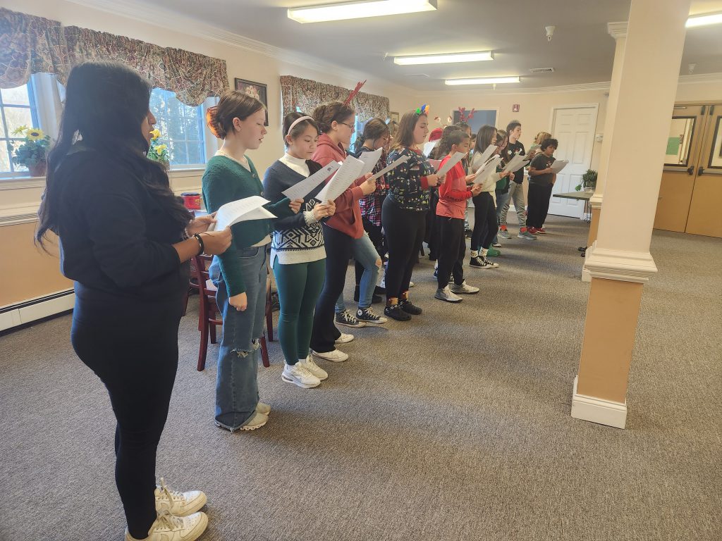 A row of middle school students stand holding papers as they sing.