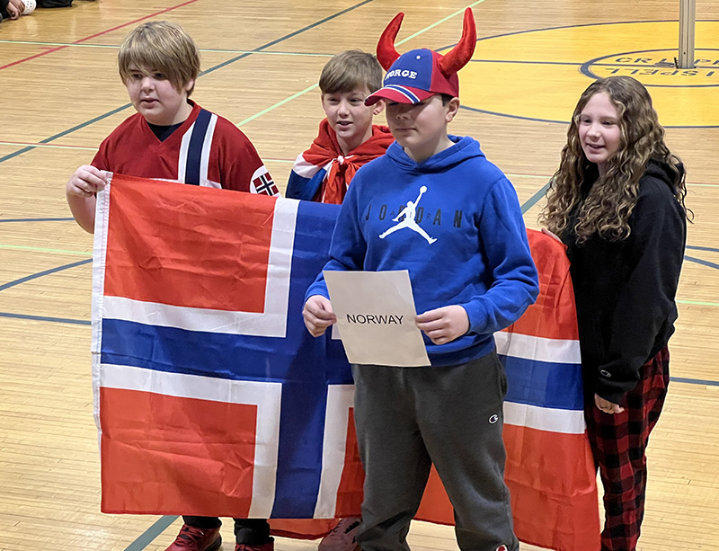Four middle school students carry the flag of Norway with one walking in front with a  viking hat on.