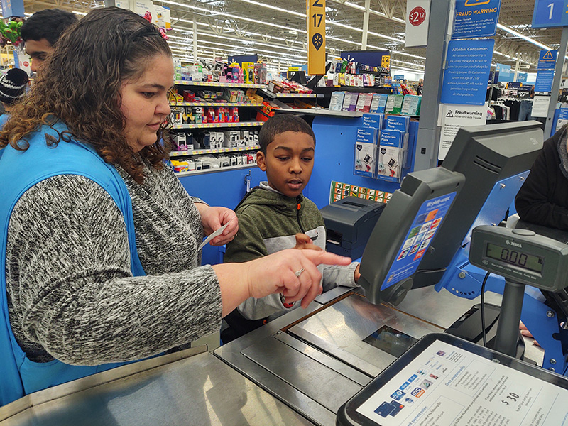 A middle school boy stands at a register in a Walmart with a woman who is pressing the screen.