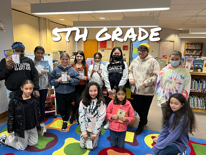 A group of 12 fifth grade students - four kneeling in front and eight standing behind them - all holding books.