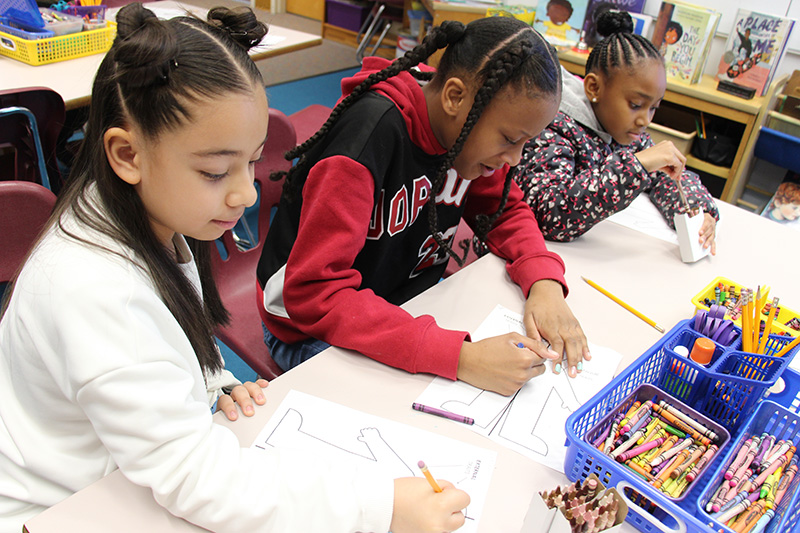 A table with three fourth-grade girls working at it. they are coloring and writing on a picture.