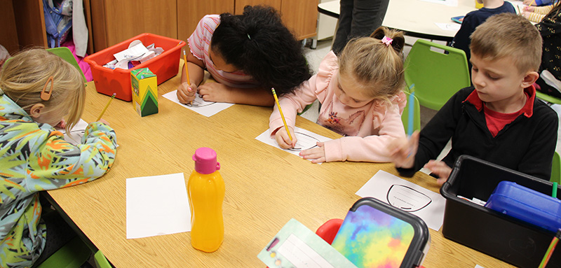 A table of smaller elementary students all drawing and coloring at a table.