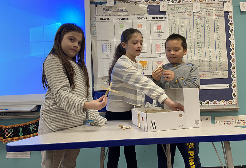 Three fourth-grade students show their wigwam structure they built.