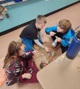 The photo is taken from above as three fourth-grade students work on their wigwam and longhouse project.