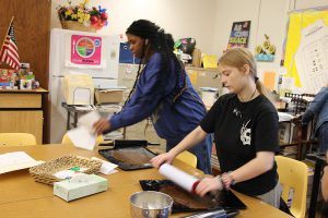 Two high school age girls roll out gingerbread dough.