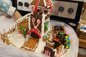 A gingerbread house - a slender one with a raised roof decorated with red licorice, and several little train cars on the side.