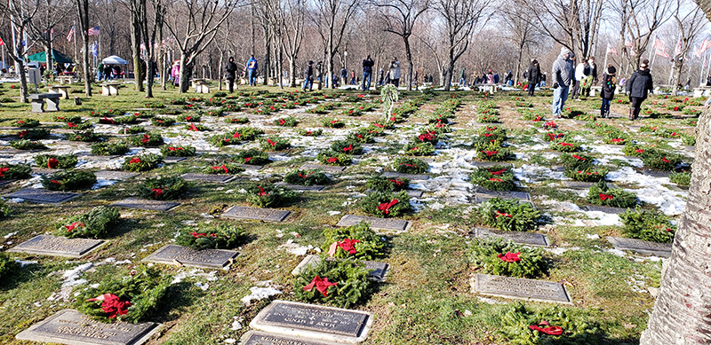 Rows of military graves with some snow in between some of them. On each gray granite grave is a green wreath with a red bow.