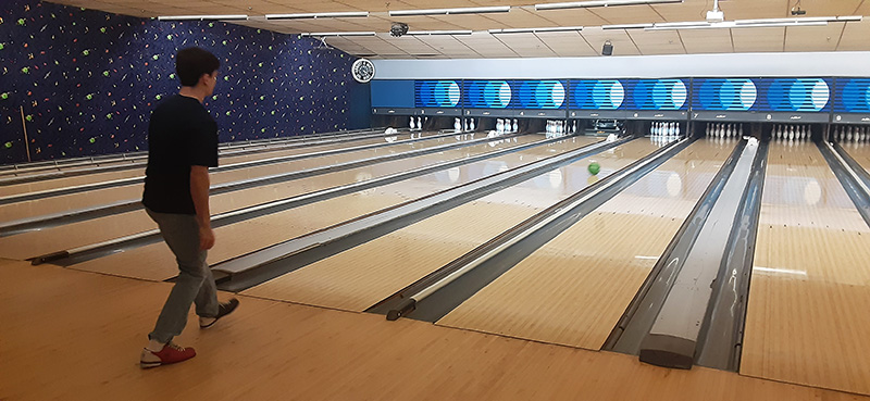 A young man wearing dark clothes just released a bowling ball down the alley.