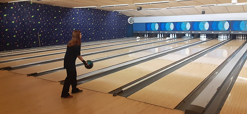 A young woman wearing dark clothes just released a bowling ball down the alley.