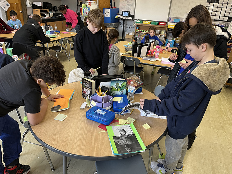 A round table with several fourth graders standing at as they read books they wrote.