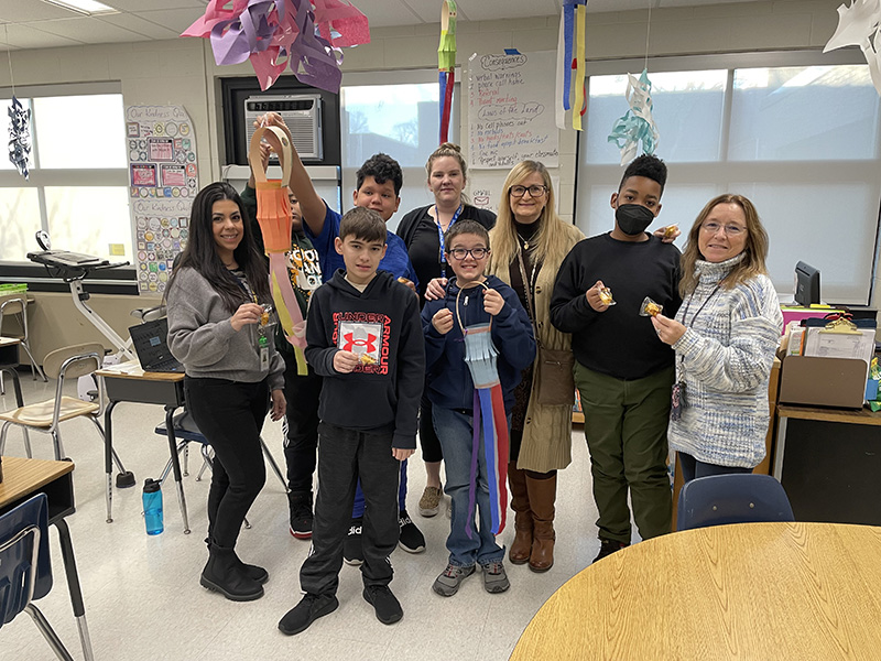 A group of five sixth-grade students stand with four adult women. Two of the students on the left are holding a Chinese lantern they made.