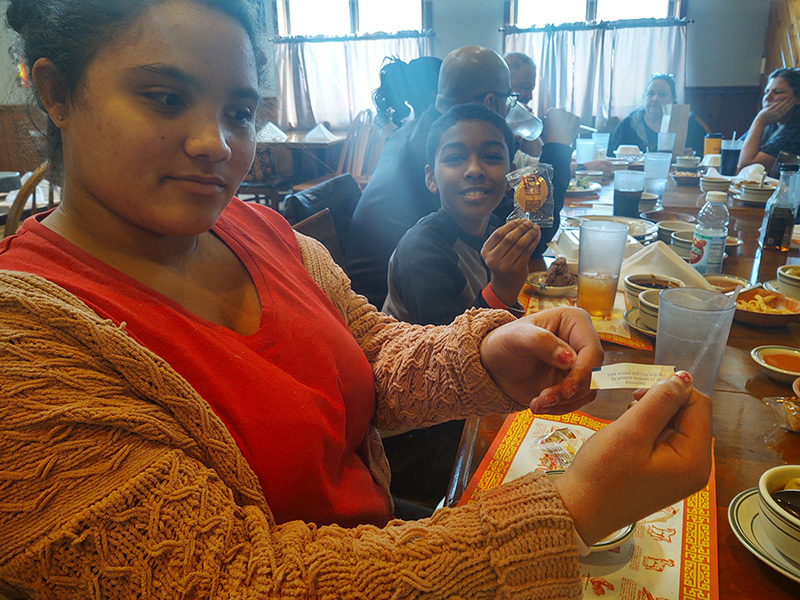 A young woman holds a fortune from a fortune cookie out in front. Next to her is  a boy  smiling.