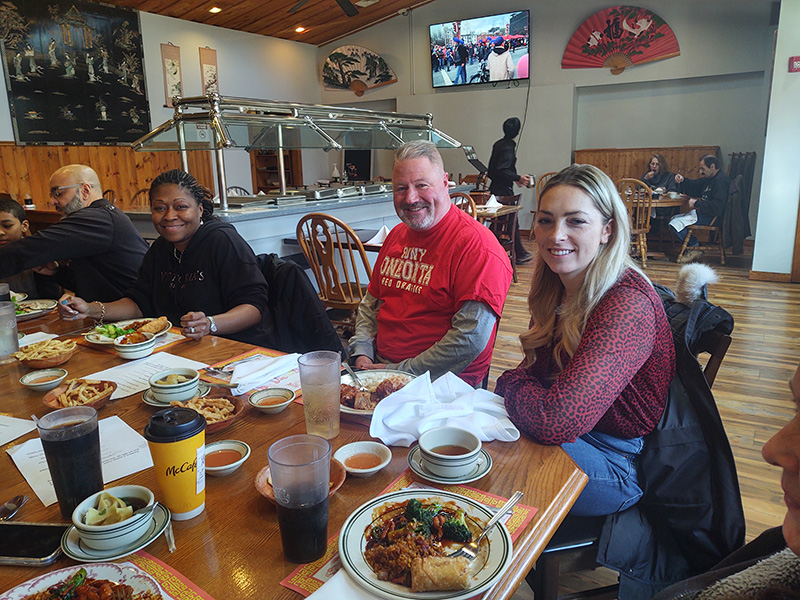 Three adults sit at a table of Chinese food smiling.