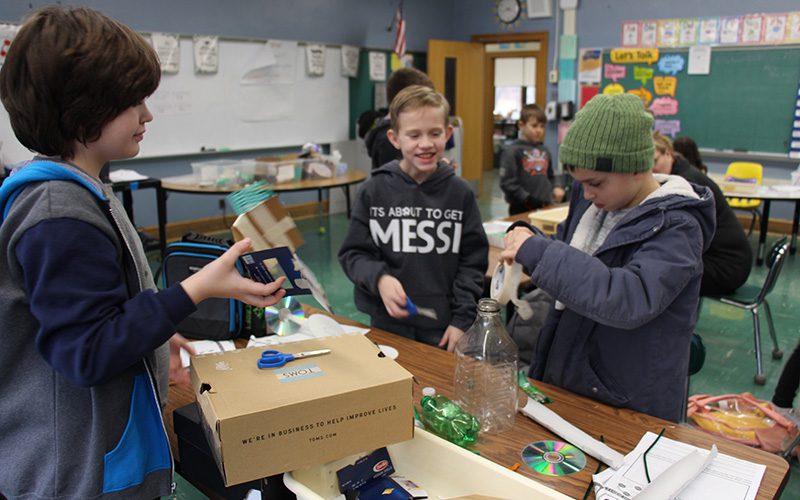 A group of three fourth-grade boys work together making a car from recycled materials.