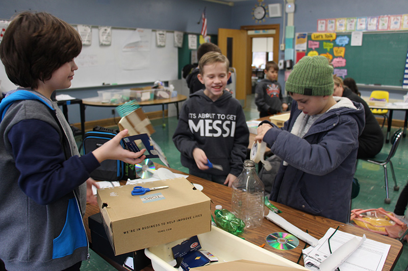 Three fourth-grade boys work together on using recyclables to create a car.