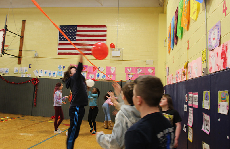 Older elementary students play volleyball with a red balloon.