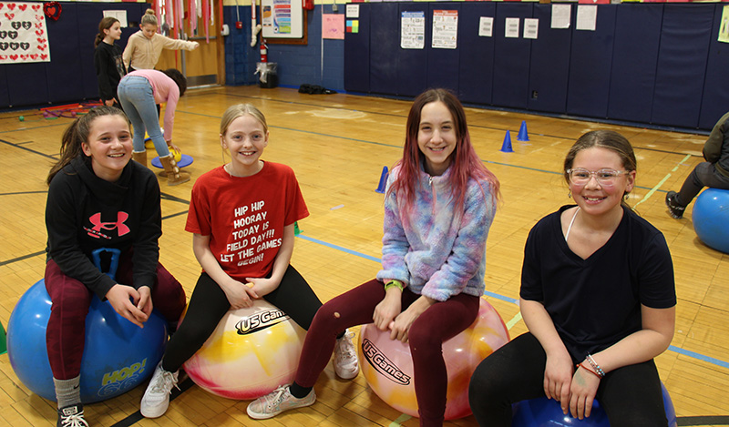 Four elementary girls sit on top of hoppity balls and smile.
