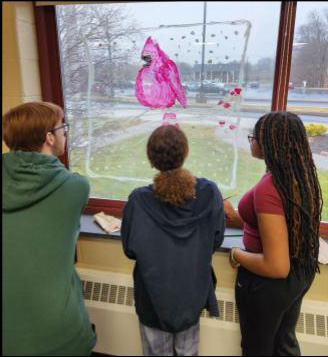 Three high school students stand and paint a large window.
