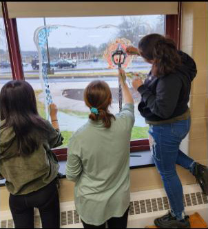 Three high school students paint a large window.