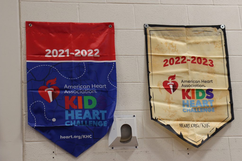 Two banners hanging on a wall. One says 2021-2022 Kid Heart Challenge and is red and blue. The other is tan colored and said Kids Heart Challenge American Heart Association.